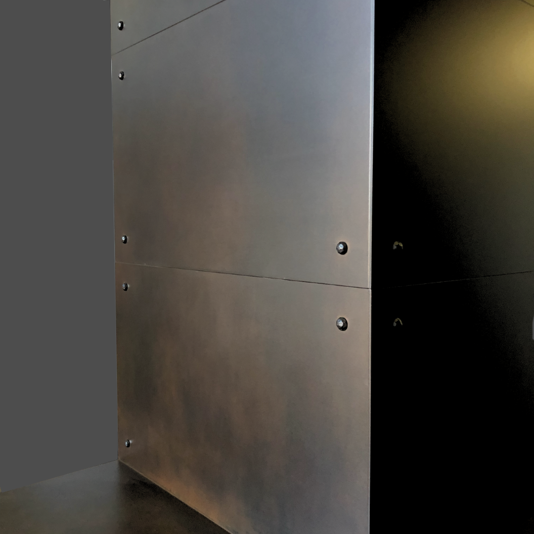 A close-up of Oil Rubbed Iron 1 shows smooth, dark metallic panels joined by visible screws against a plain gray background, with lighting that highlights its sleek, industrial design.