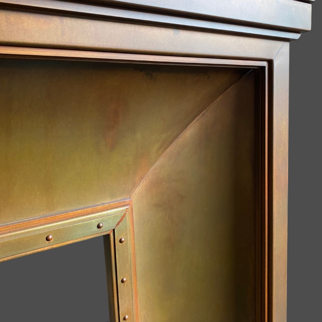 Penny Iron 1 Close-up of Penny Iron 1’s metallic corner, showcasing a bronze, slightly weathered finish with edge rivets and smooth, angular surfaces set against a plain gray background.