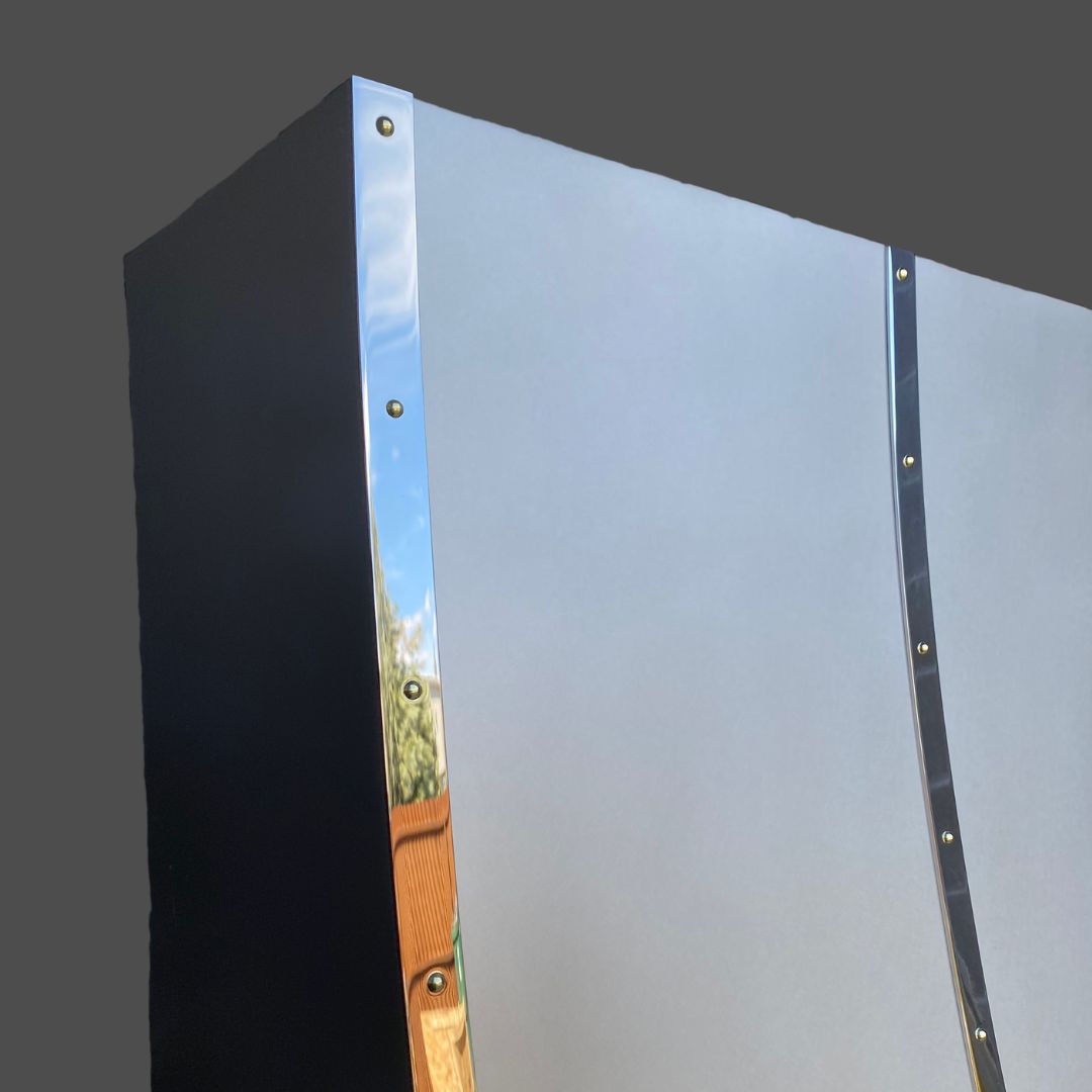 A close-up of the corner of the Pewter Burnished 2, a black rectangular item with shiny metallic strips and visible bolts along the edges, set against a plain gray background.