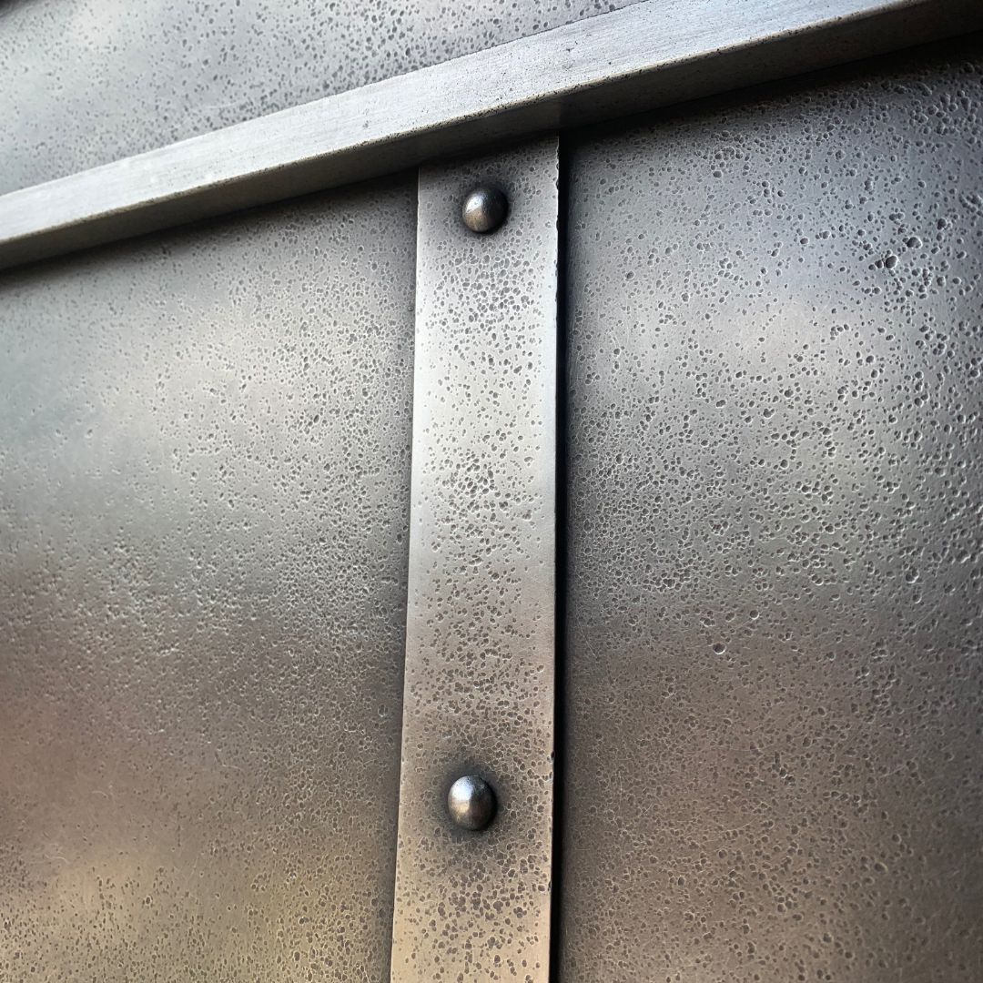 Close-up of Pewter Butterdish 1’s metallic surface featuring a vertical strip secured by two round rivets, with a textured, slightly bumpy finish and intersecting horizontal elements.
