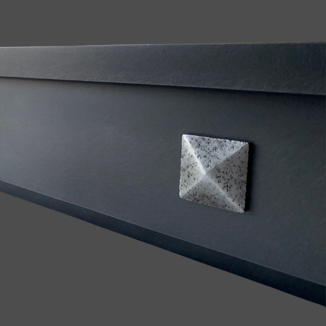 Pewter Cast 2 The Pewter Cast 2 features a textured, metallic pyramid-shaped button set on a smooth, dark gray surface with a modern, minimalist design.