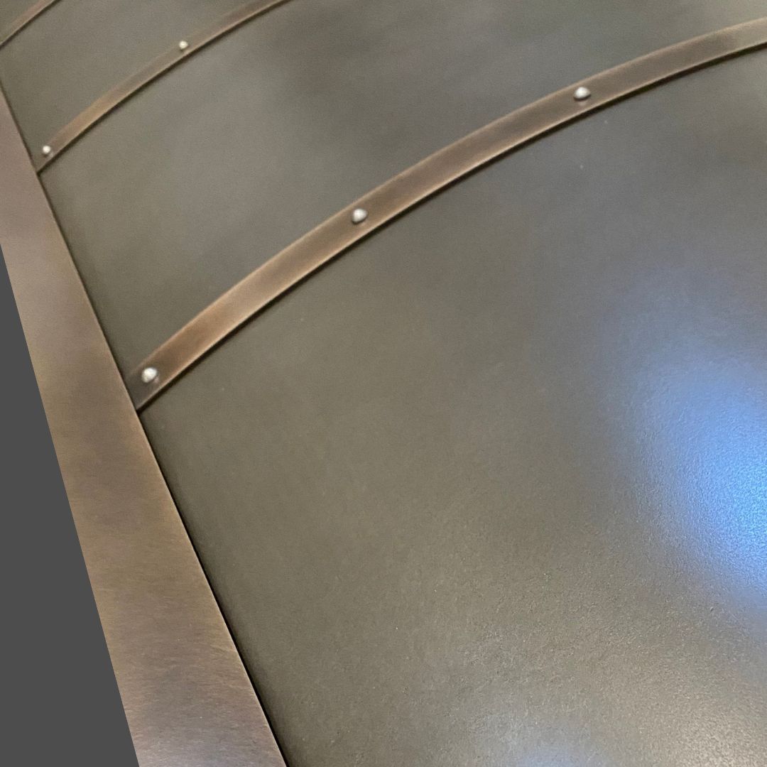 Pewter Cast 3 Close-up of Pewter Cast 3’s matte metal surface with curved bronze-colored straps and rivets, forming a segmented look. Lighting on the right creates a subtle reflection.
