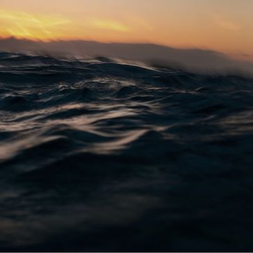 Rustic Reclaimed 1-2 Rustic Reclaimed 1-2 features dark, choppy ocean waves in the foreground beneath a soft orange and yellow sunset sky, with distant clouds lining the horizon in the background.