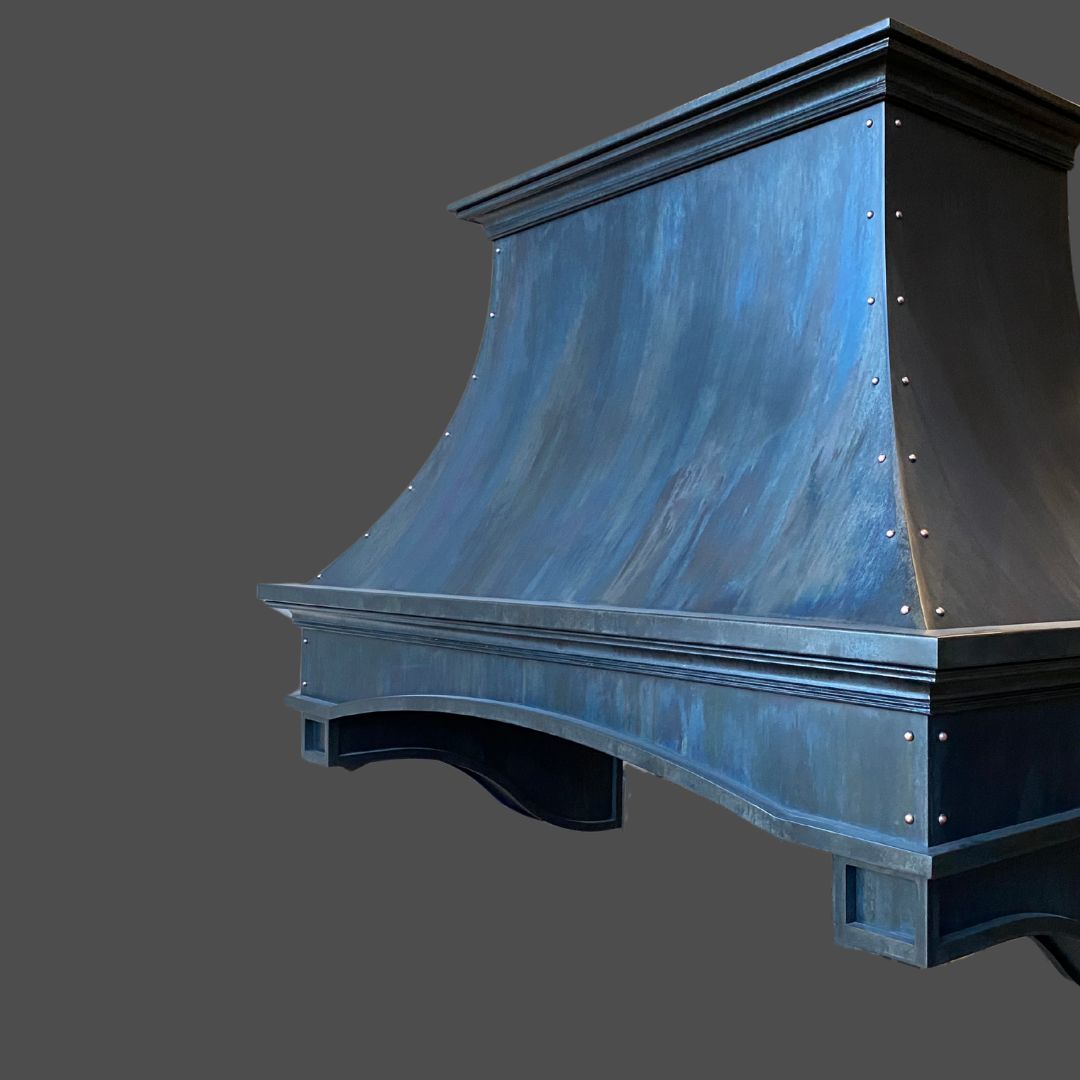 Slate 2 The Slate 2 is a blue metallic range hood featuring a curved, flared design with decorative trim and visible edge rivets. Its brushed, textured finish stands out against a plain gray background.