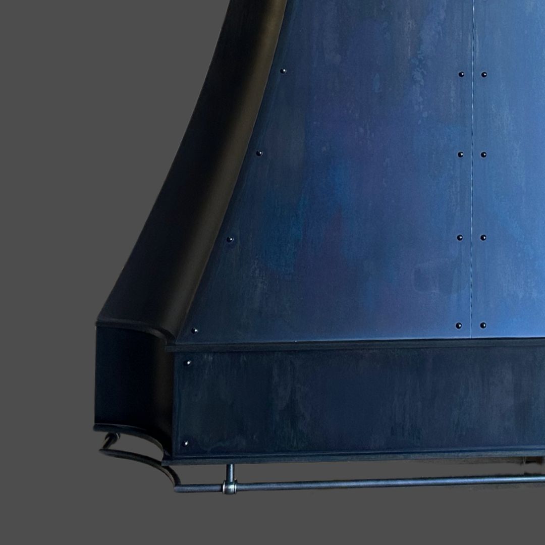 Slate 3-3 A close-up of the Slate 3-3, a modern matte black metal range hood featuring a sloped design and visible rivets, set against a plain gray background.