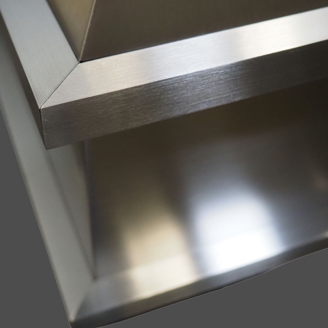 Close-up of Stainless Grained 2 brushed stainless steel surfaces intersecting at sharp angles, highlighting clean lines and a modern metallic finish against a gray background.