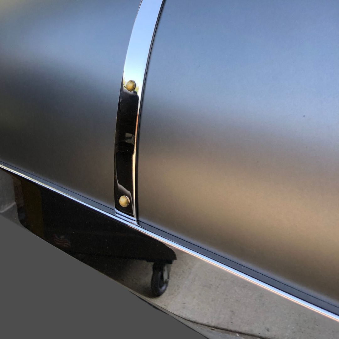 Stainless Polished 3-2 Close-up of the Stainless Polished 3-2 grill, featuring a matte black metal body, curved lid, shiny chrome trim, and two brass rivets placed outdoors on concrete.