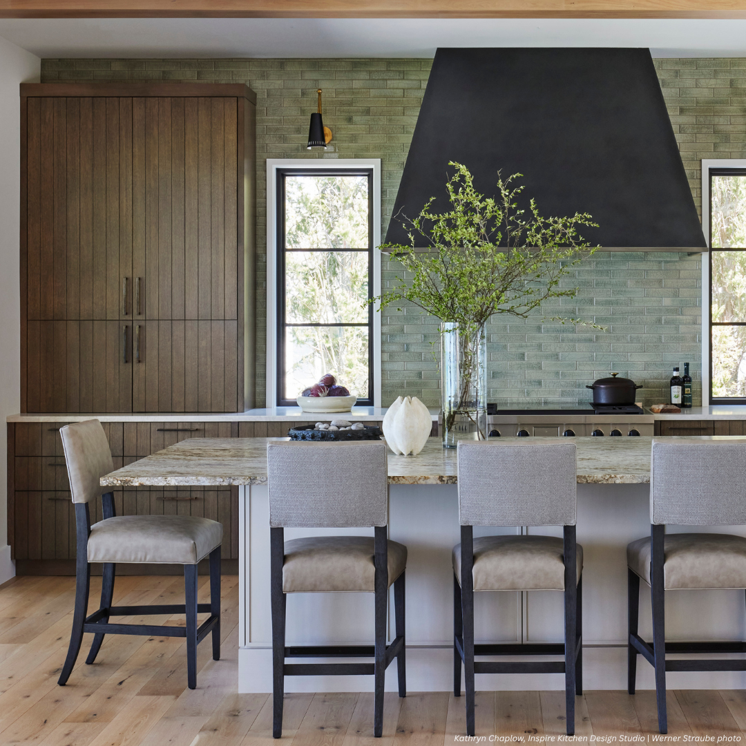 The Tabernash gallery1 features a modern kitchen with a large island, beige upholstered chairs, green tile backsplash, wooden cabinets, black range hood, two windows, and a vase with green branches on the counter.