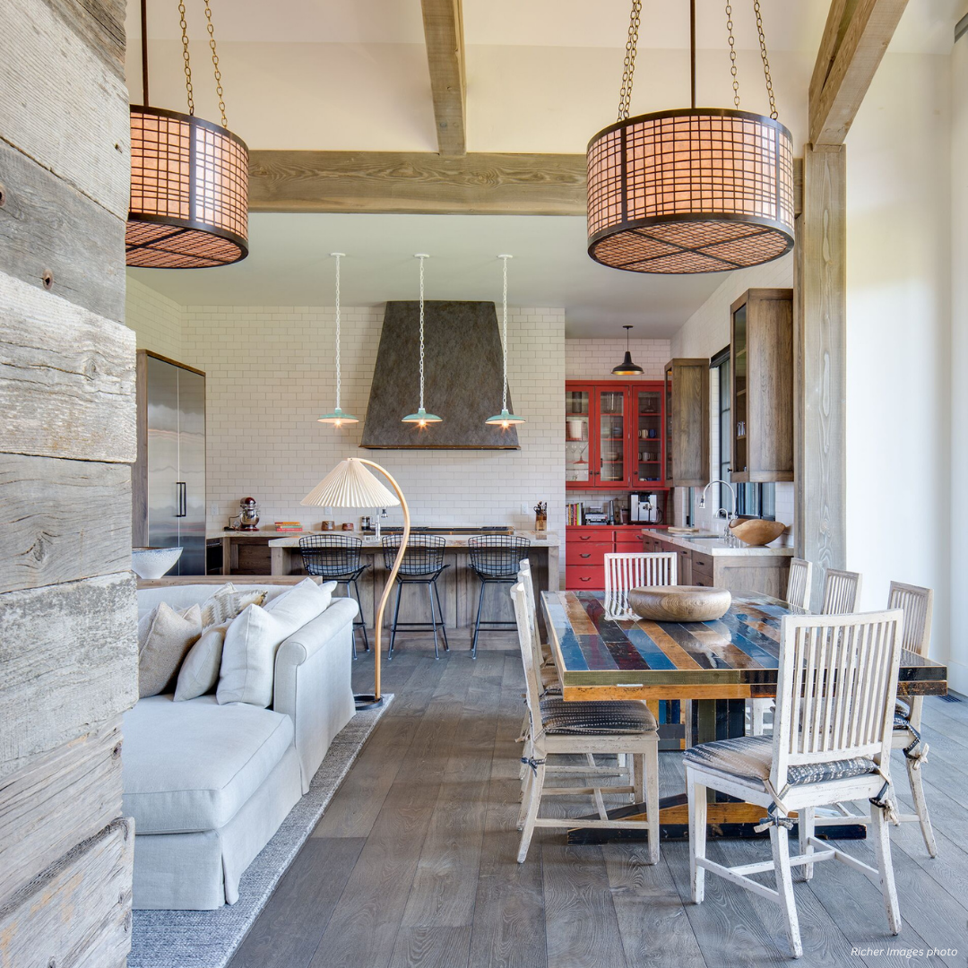 Tabernash gallery2 features an open-concept kitchen and living area with rustic wood accents, a striped dining table, mismatched chairs, pendant lights, and a cozy gray sofa. Tall windows fill the space with light, enhancing the modern-rustic decor.