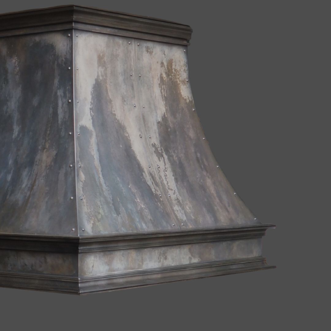 The Vintage Reclaimed 2 is a metal range hood with a weathered gray and brown finish, rivet accents, and a flared rectangular design, showcased against a plain gray background.