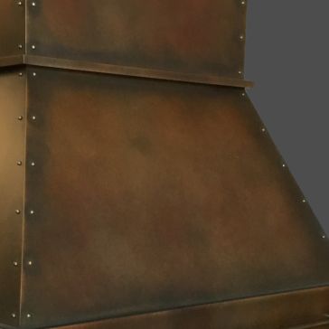 A close-up of the Warm Foundry 3 metal vent hood showcases its dark rustic finish, visible rivets, and subtly weathered look against a plain gray background.