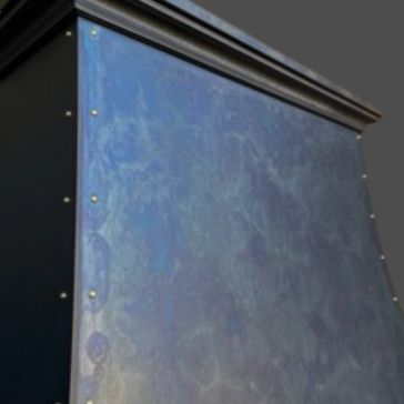 Close-up of the Winter Blue 5720 (3) showing a metallic surface with blue and purple iridescence, rivets along the edges, and decorative molding at the top, set against a plain gray background.