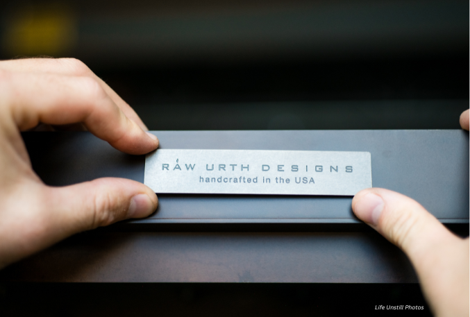 Close-up of two hands holding the "handcrafted in the usa 1" metal label against a blurred background.