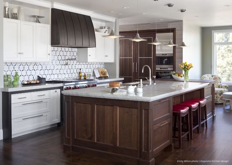Raw Urth Snowmass Modern kitchen featuring Raw Urth Snowmass, white upper cabinets, dark lowers, hex tile backsplash, stainless appliances, large marble island with dark wood base, red barstools, and overhead pendant lights.