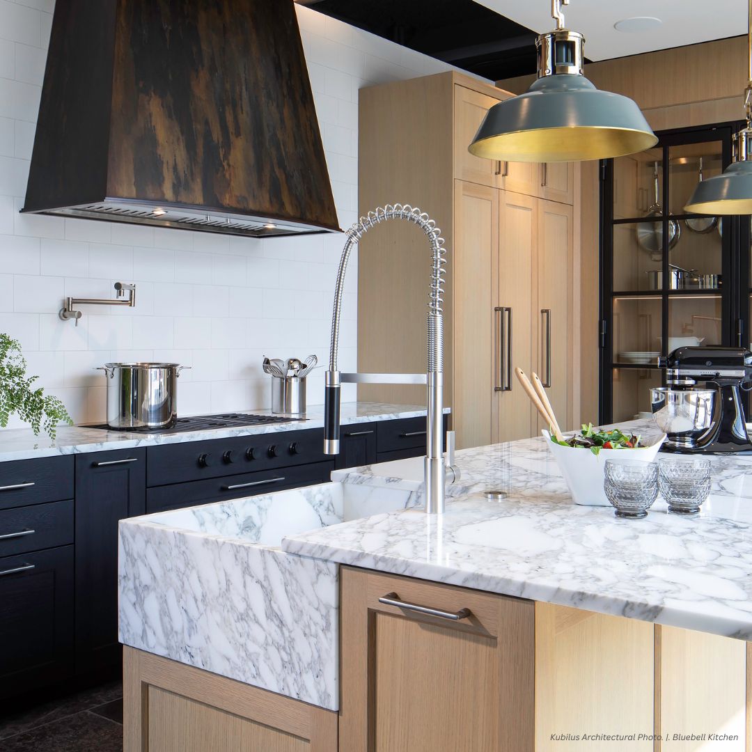 Modern kitchen featuring the predesigned hood portfolio_raw by Urth Designs, stainless steel appliances, black and wood cabinetry, a marble island with pendant lights, plus a salad bowl and glasses on the countertop.