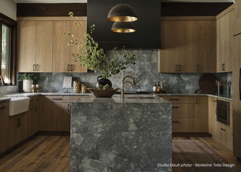 ru-box Modern kitchen featuring ru-box light wood cabinets, gray marble countertops and backsplash, a central island with gold faucet, black and gold pendant lights, and a vase of green branches. Natural light streams through the window.