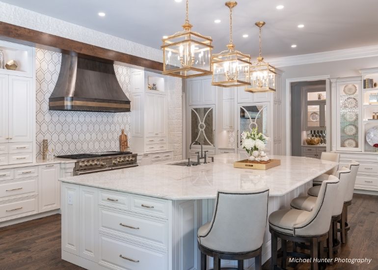 ru-custom-maryjane The ru-custom-maryjane features a spacious kitchen with a large marble island, white cabinets, stainless steel range hood, pendant lights, upholstered bar stools, and built-in shelves for décor and dishes.