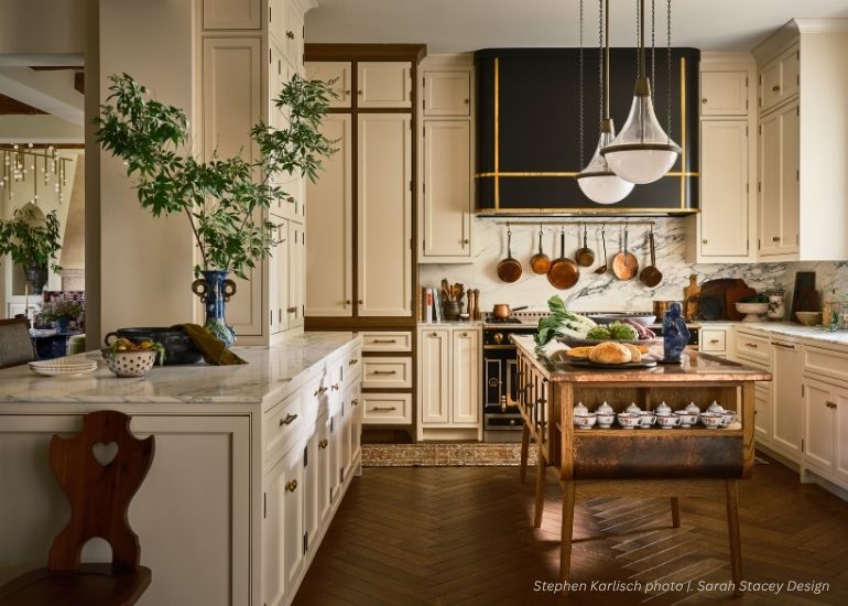 ru-portfolio-tablet An elegant kitchen features ru-portfolio-tablet alongside cream cabinets, marble counters, a wooden island with bread and veggies, pendant lights, potted plants, and copper pots above the stove.