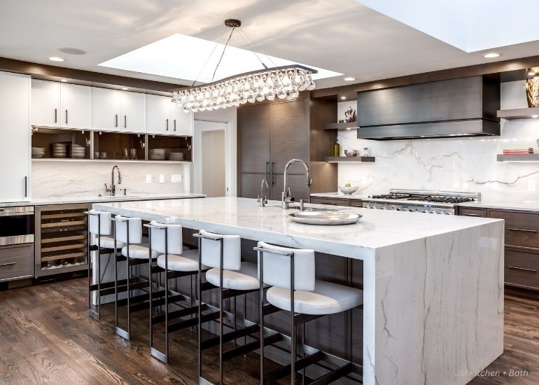 Modern kitchen with a large marble island, six white barstools, dark wood cabinets, stainless steel appliances including ru-predesigned-hoods, under-cabinet lighting, and a decorative chandelier for a sleek contemporary look.