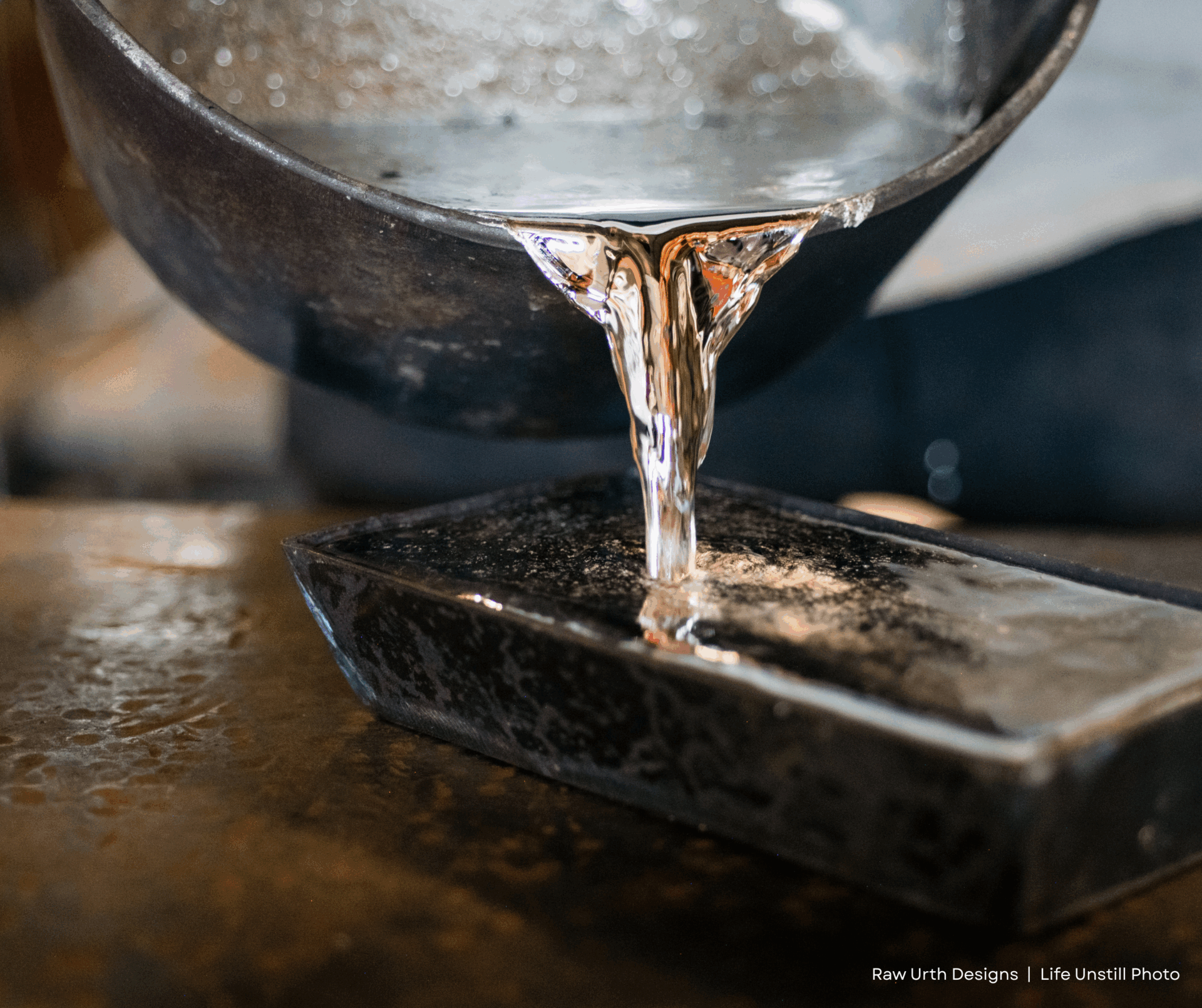 Molten metal is being poured from a heavy black crucible into a rectangular mold on a workbench, capturing the shiny, flowing liquid mid-pour with Product 2.