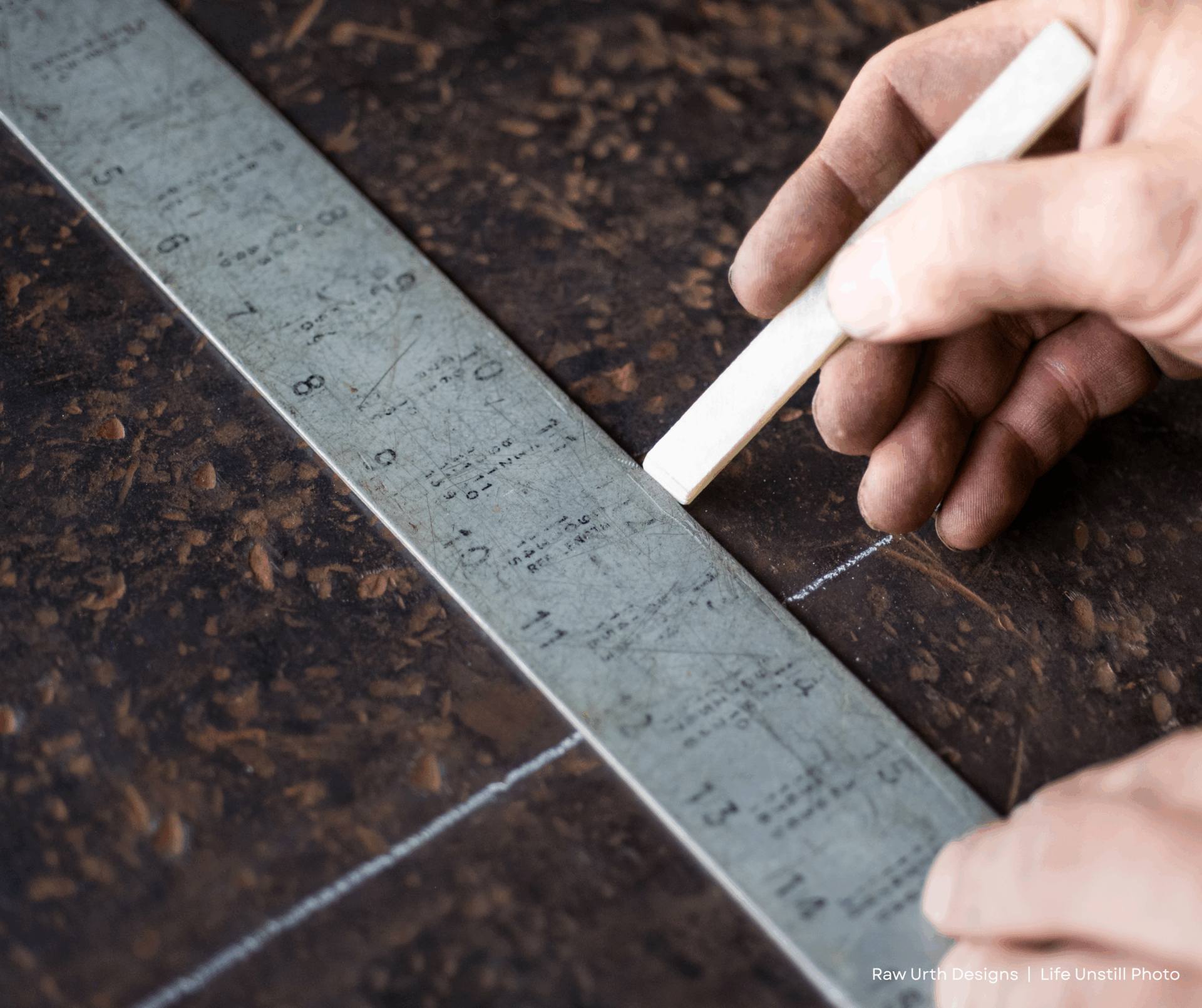 A hand uses Product 3 to draw a straight line along the edge of a metal ruler on a dark, textured surface.