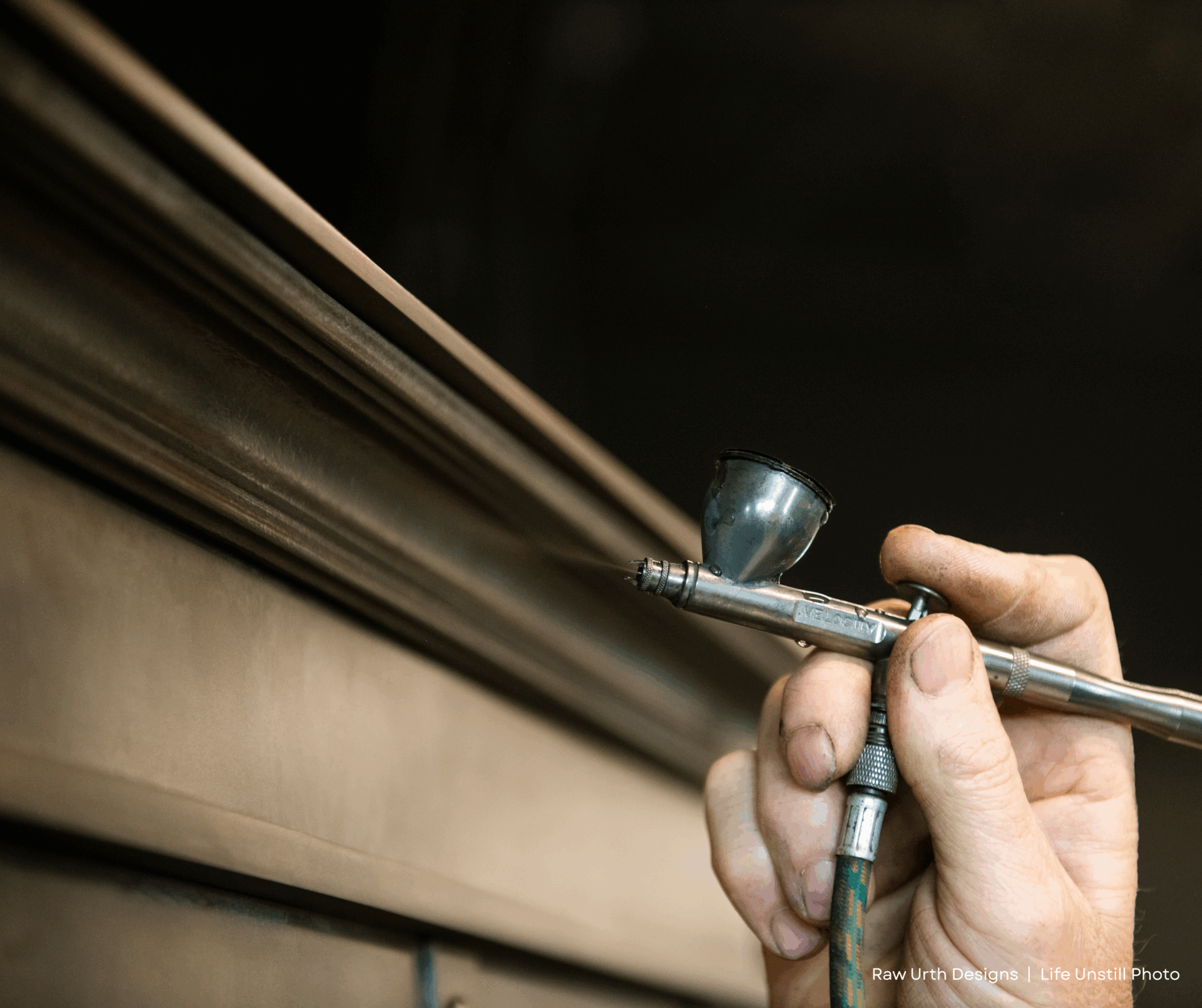 A close-up shows a hand using an airbrush tool to finish the edge of wood, highlighting www.lifeunstill.com. The background is blurred for focus on the process.