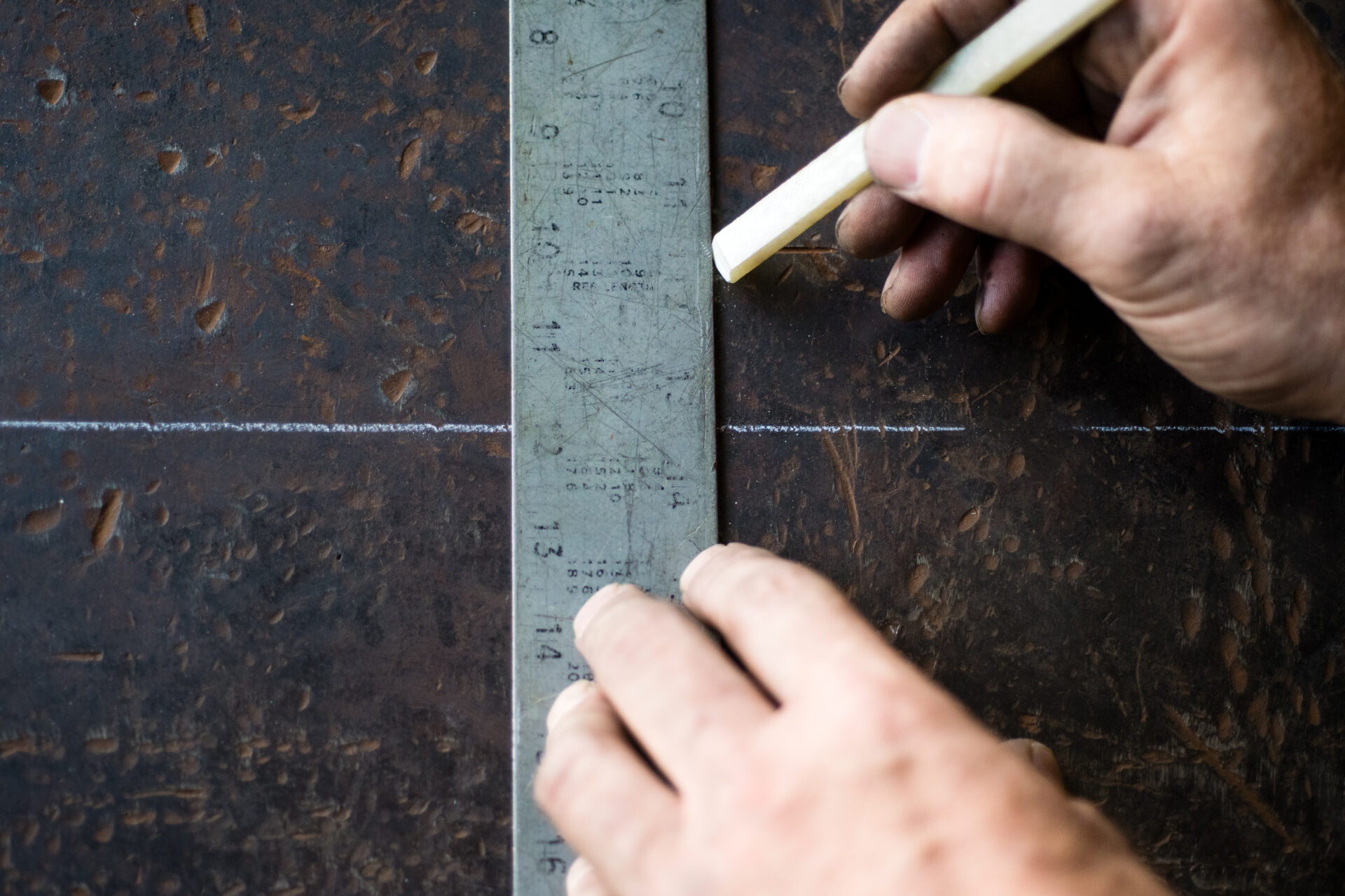 Close-up of hands using a metal ruler and chalk to draw a straight line on rusty metal, showcasing www.lifeunstill.com.