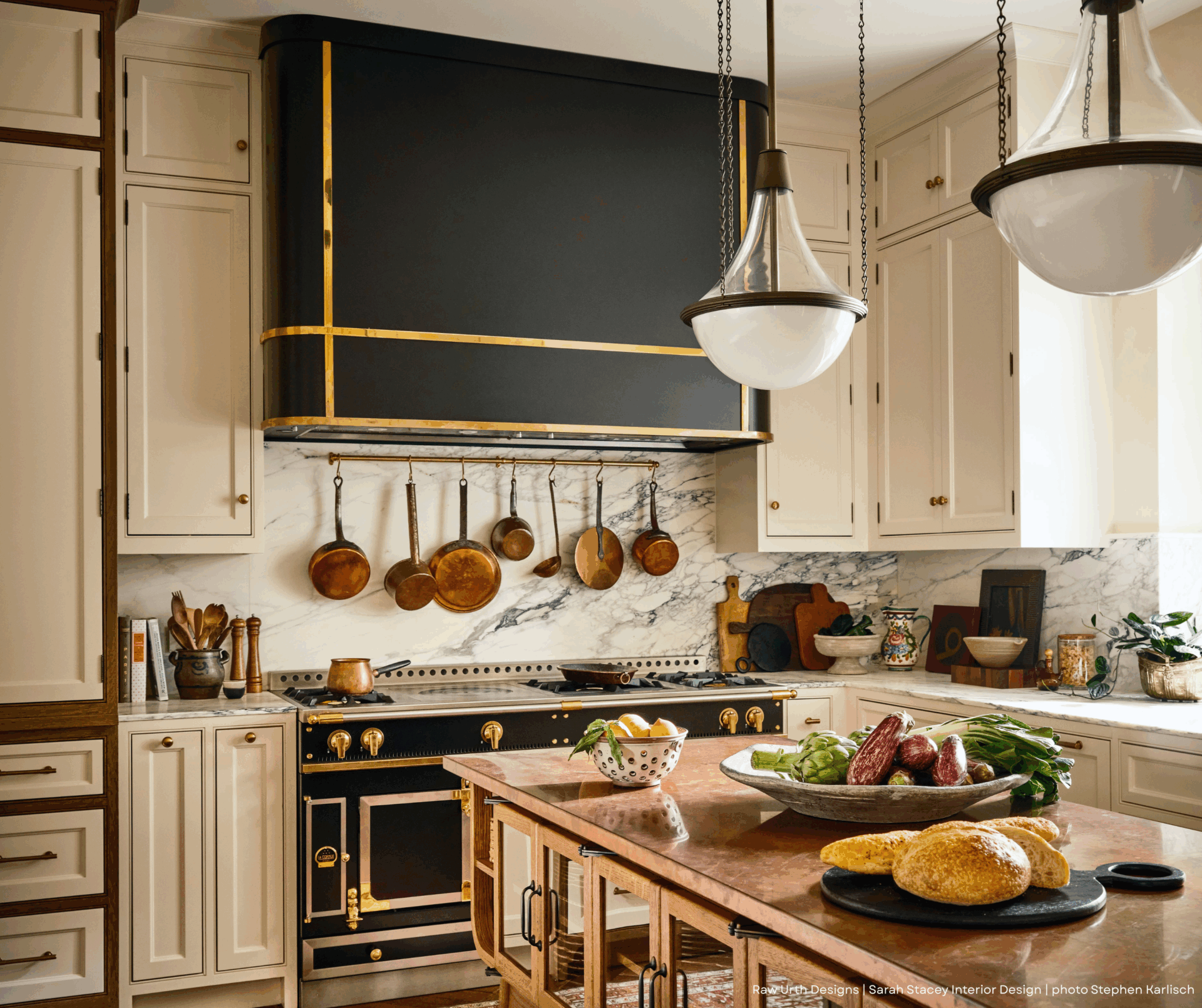 Elegant kitchen featuring Product Name: 5 with cream cabinets, marble backsplash, and copper pots. A wooden island displays fresh vegetables and bread, with pendant lights above. Sunlight pours through a nearby window.