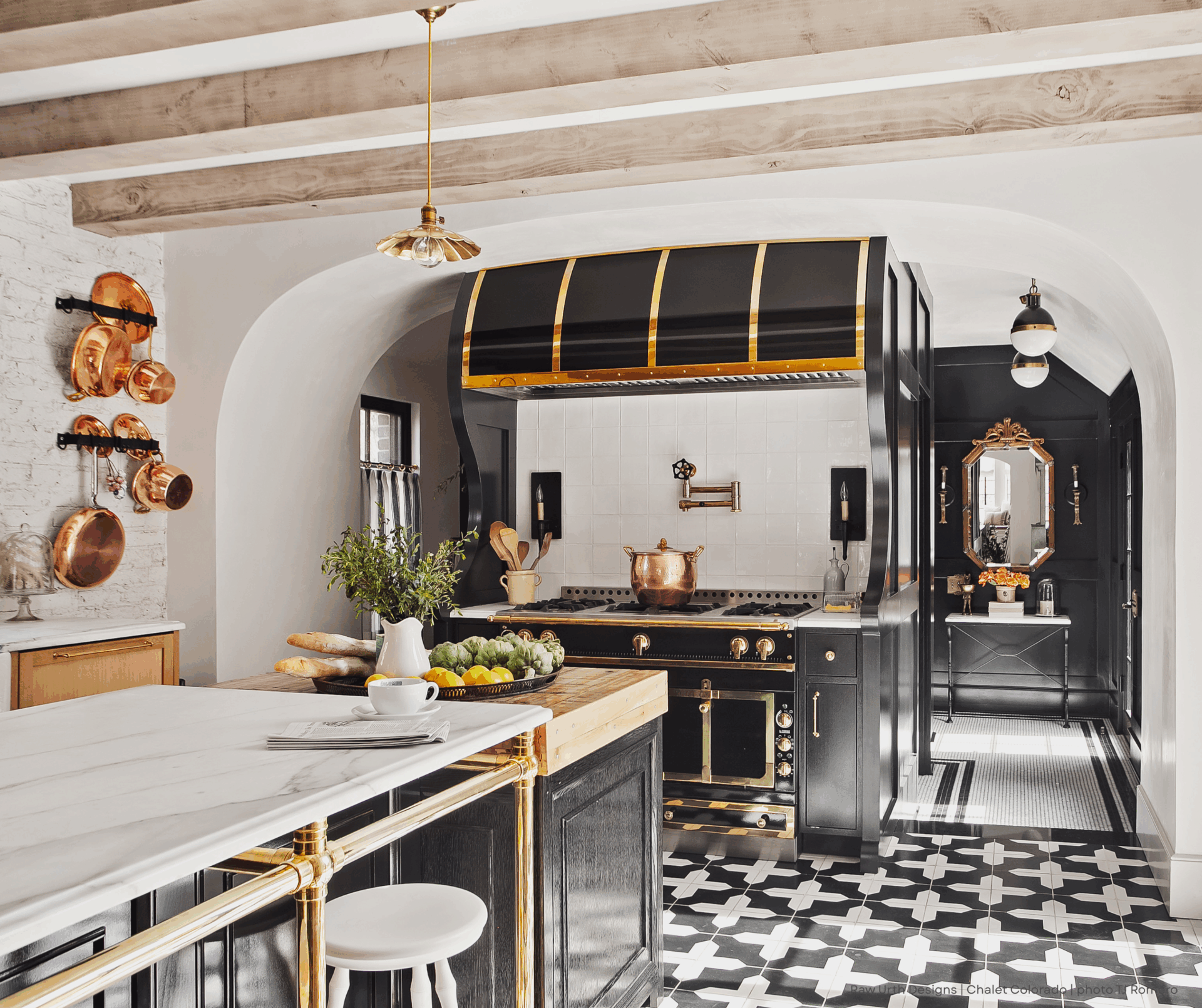 6 Elegant kitchen featuring Product 6: black and gold accents, a marble island, copper pots on white brick walls, patterned floor tiles in black and white, and a vintage stove under a matching black hood.