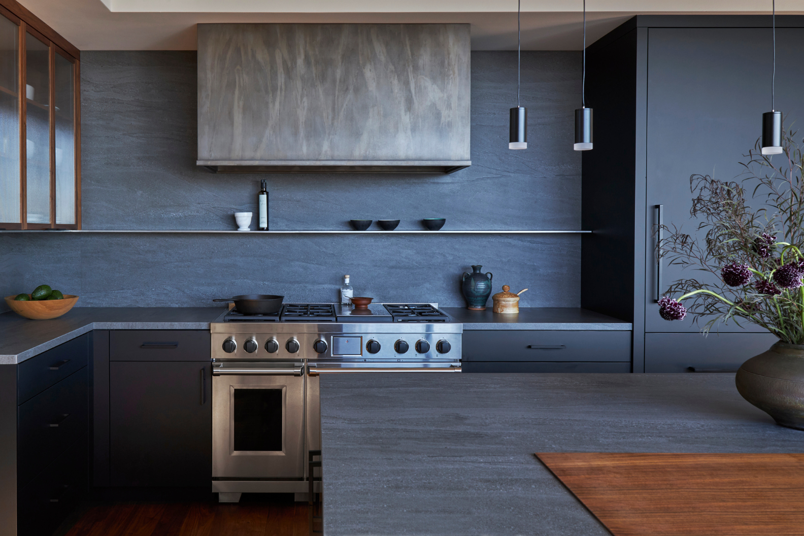 Product 12 features a sleek modern kitchen with dark gray cabinets, stainless steel stove and hood, minimalist shelving for dishes, and a kitchen island with a wooden inlay topped with dark flowers—perfect for contemporary spaces.
