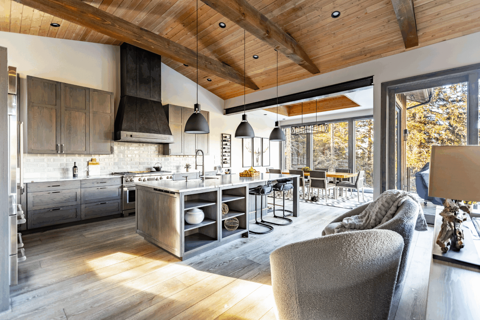 Product 4 features a modern rustic kitchen with wooden beams, gray cabinets, a spacious island with stools, pendant lighting, stainless steel appliances, and an open dining area highlighted by large windows for natural light.