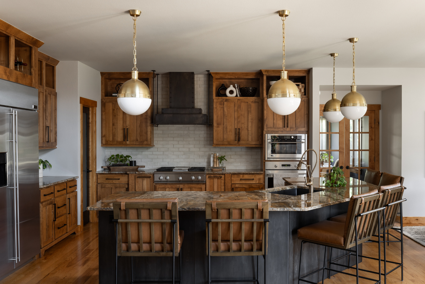 Product 7: Modern kitchen featuring wooden cabinets, stainless steel appliances, a spacious marble island with sink, four high-backed chairs, pendant lighting overhead, and decorative potted plants.