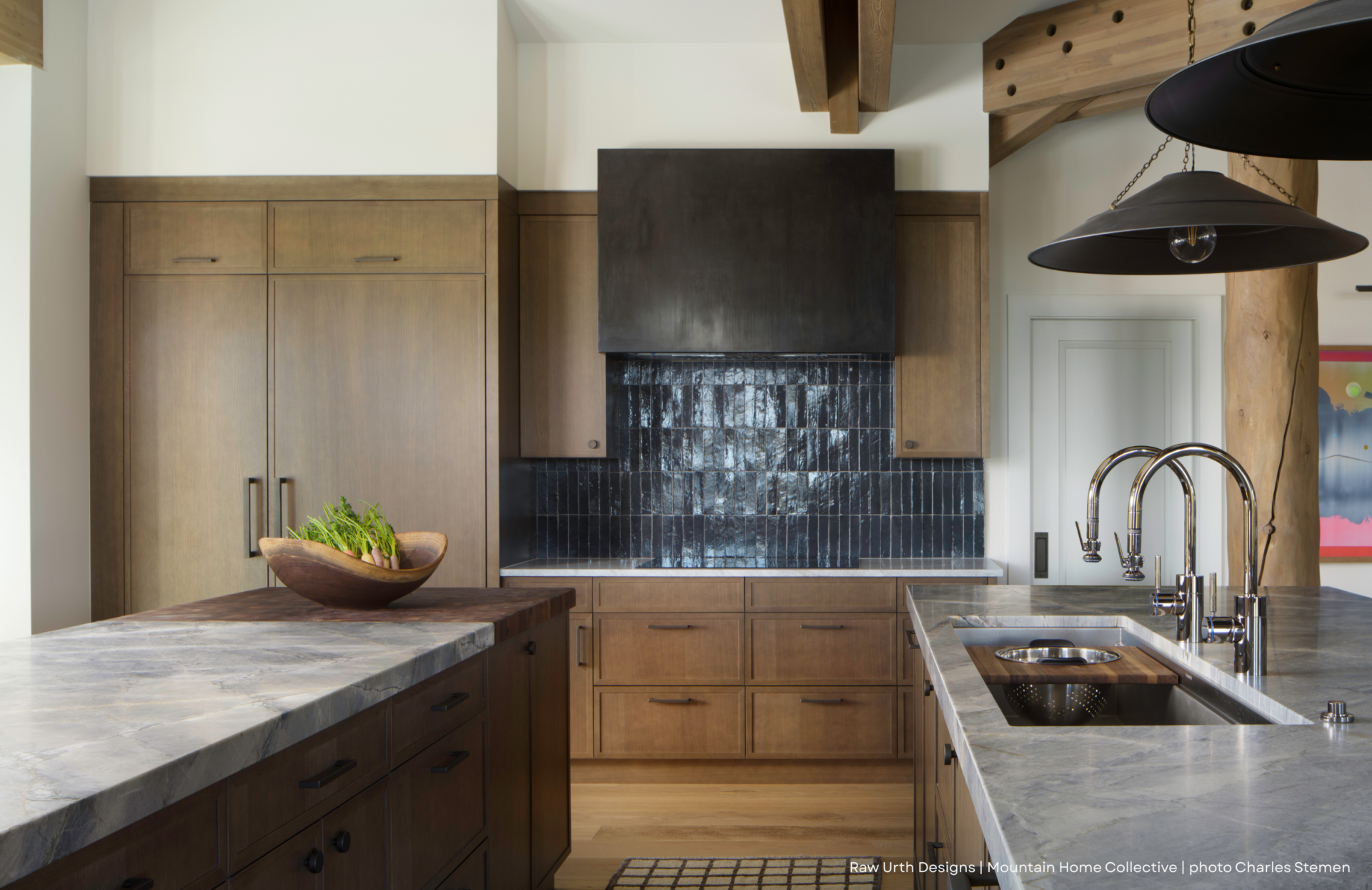 Modern kitchen featuring wood cabinets, a spacious island with stone countertop, black tile backsplash, stainless steel sink, wooden bowl with greenery, black pendant light, and rustic wooden beams. RU_Blog Images highlights the design.