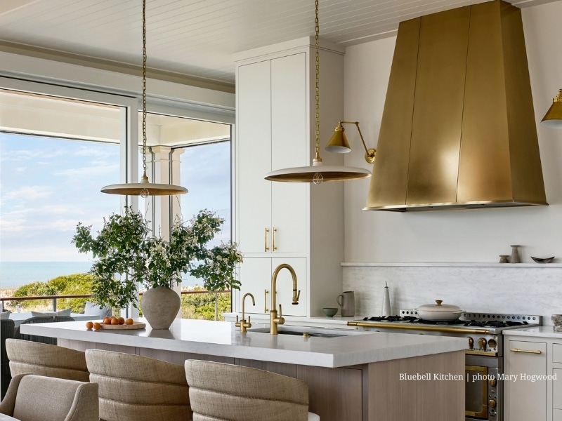 The Aspen kitchen features wooden cabinets, a spacious island with seating for four, pendant lighting, black countertops, a white subway tile backsplash, and large windows that fill the space with natural light.